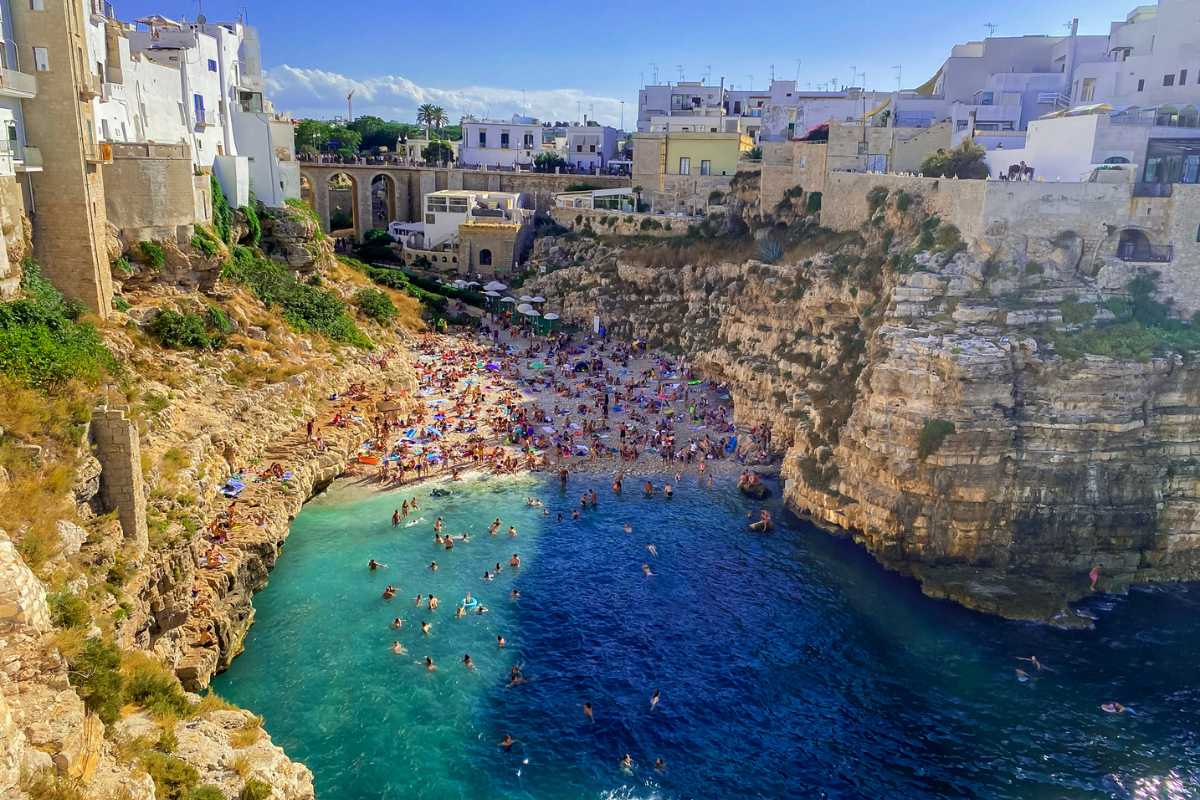 Primo piano di un treno regionale Trenitalia in arrivo alla stazione di Polignano a Mare, sullo sfondo il borgo bianco e il mare