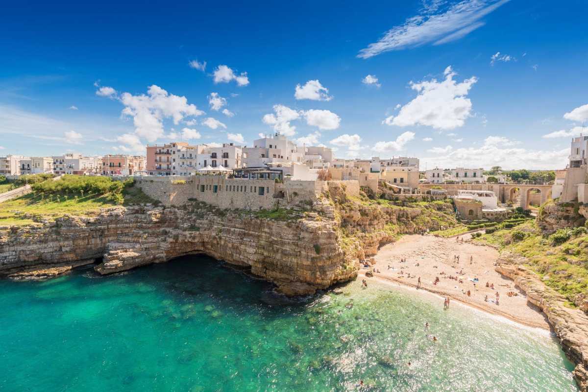 Vista panoramica di Polignano a Mare al tramonto durante una festa tradizionale, con luci colorate, folla e bandiere tipiche