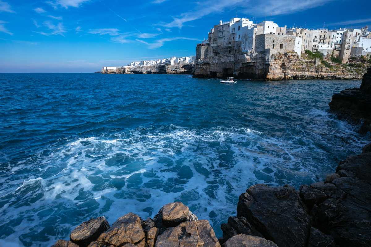 Panoramica della costa di Polignano a Mare all’alba, con le case bianche arroccate sulla scogliera e il mare calmo in primo piano